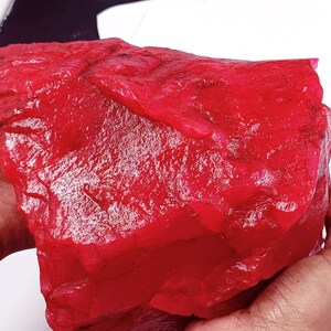Könnte beinhalten: Ein großer, roher, roter Rubin-Edelstein. Der Rubin hat eine tiefe, satte rote Farbe und eine natürliche, unpolierte Oberfläche.