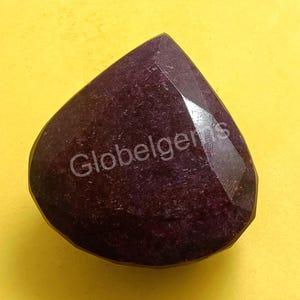 May include: A deep purple gemstone with a faceted, teardrop shape. The gemstone is cut and polished, and has a smooth, glossy finish.