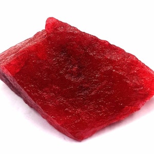May include: A large, rough, red ruby gemstone. The ruby has a deep, rich red colour and a slightly translucent appearance.