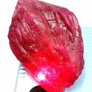 Peut inclure: Une grosse pierre précieuse de rubis rouge brute avec une couleur profonde et riche. La pierre précieuse a une finition naturelle non polie.