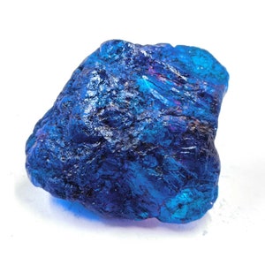Puede incluir: Una piedra preciosa en bruto y sin pulir de un color azul profundo y vibrante. La superficie de la piedra es irregular y texturizada, con varias facetas y estructuras cristalinas que reflejan la luz, creando tonos azul marino y cobalto.