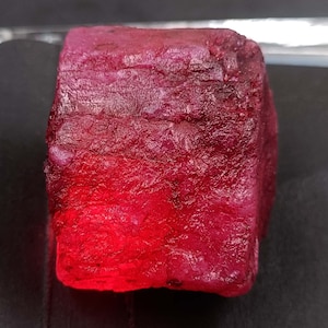 Könnte beinhalten: Ein großer, tiefroter Rubin mit einer rauen, facettierten Oberfläche.