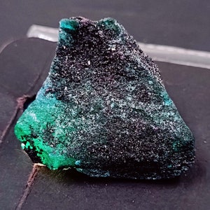 May include: A dark green and black rough gemstone with a speckled texture.