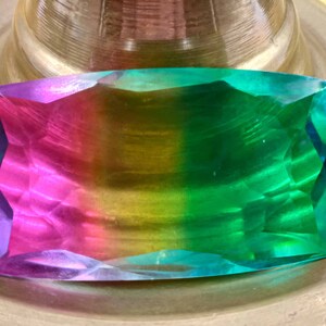 May include: A large, rectangular, faceted gemstone with a rainbow of colors, including purple, pink, yellow, green, and blue.
