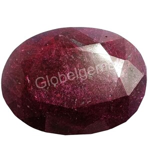 May include: A deep red oval-shaped gemstone with a faceted cut. The gemstone has a slightly translucent appearance with a hint of purple.