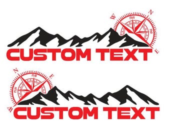 Puede incluir: Dos calcomanías de silueta de cordillera negra con una brújula roja y el texto "CUSTOM TEXT" en rojo.