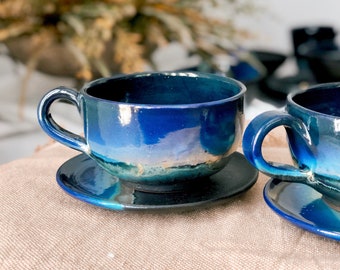 May include: Two blue ceramic teacups with matching saucers. The cups have a glossy finish and a blue and green ombre design.
