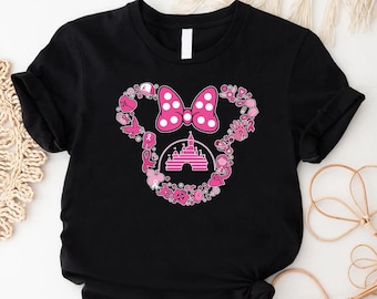 May include: Black t-shirt featuring a pink Minnie Mouse design. The design includes a polka dot bow, a castle, and various pink elements forming the mouse's silhouette. The shirt is made of a soft material.