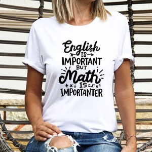 May include: A white t-shirt with the text "English is important but Math is importanter" in black. The person is sitting in a woven chair. The shirt has a crew neck and short sleeves.