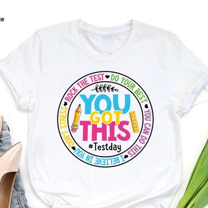 May include: White t-shirt with a colorful graphic that says "You Got This" with a pencil, ruler, and the hashtag #Testday. The shirt also has the phrases "Rock the test", "Do your best", and "I believe in you".