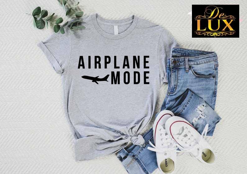 Puede incluir: Una camiseta gris claro con las palabras "AIRPLANE MODE" y la silueta de un avi&oacute;n. La camiseta se combina con vaqueros azules y zapatillas blancas. Se ve una ramita de vegetaci&oacute;n.