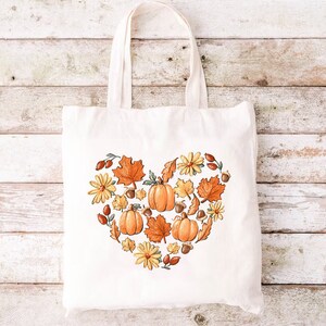 a white tote bag with a heart made of pumpkins and leaves