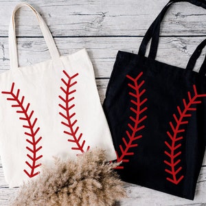 May include: Two tote bags, one cream and one black, each featuring a red baseball stitch design. The bags have long handles and are made of a sturdy fabric, perfect for carrying groceries or other items.