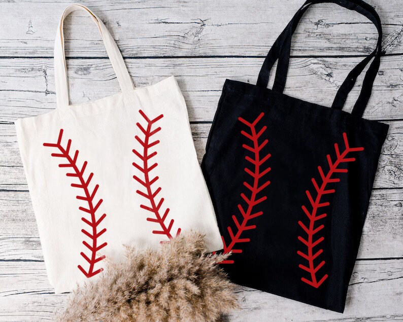 May include: Two tote bags, one cream and one black, each featuring a red baseball stitch design. The bags have long handles and are made of a sturdy fabric, perfect for carrying groceries or other items.