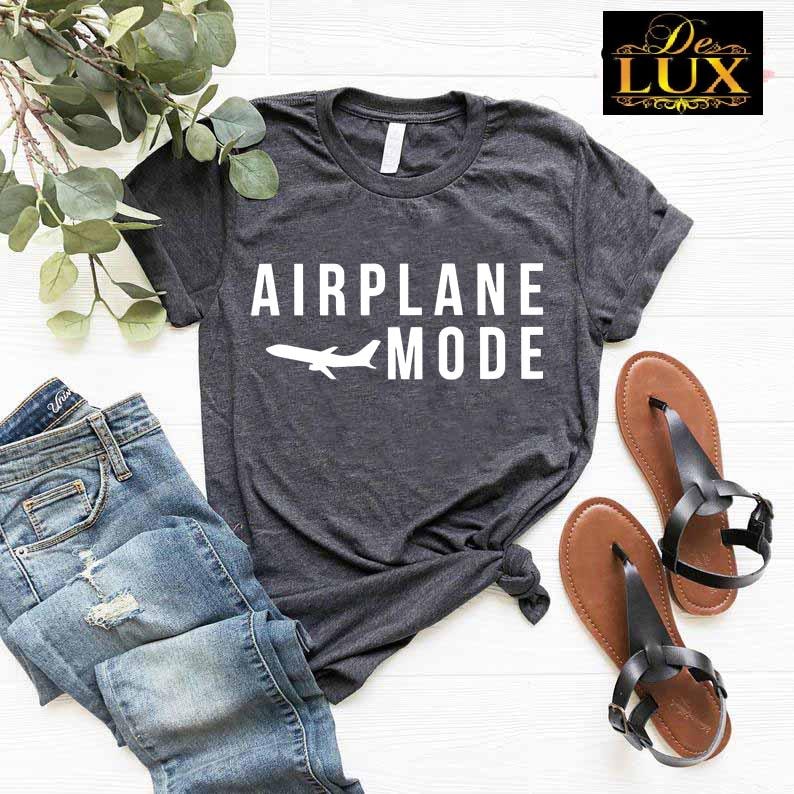 Puede incluir: Una camiseta gris oscuro con las palabras "AIRPLANE MODE" y un gr&aacute;fico de avi&oacute;n blanco. La camiseta se combina con vaqueros azules y sandalias marrones con correas negras. La imagen est&aacute; estilizada sobre una superficie blanca.