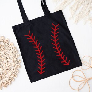 May include: Black tote bag with red baseball stitching design. The bag has two long handles and is made of a durable fabric. The baseball-themed design is a bold and eye-catching detail.