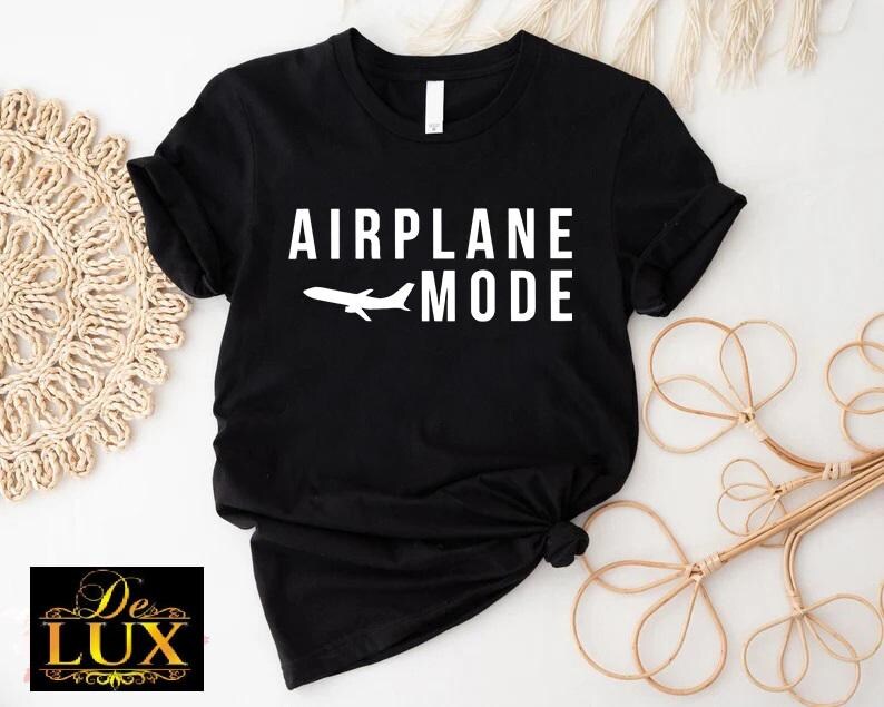Puede incluir: Camiseta negra con las palabras "AIRPLANE MODE" en blanco y un avi&oacute;n blanco. La camiseta est&aacute; anudada en la parte inferior. El logotipo de De Lux est&aacute; en la esquina inferior izquierda.