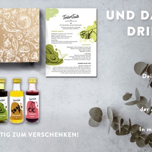 May include: A gift box set of five small glass bottles containing premium oils and vinegars. The bottles are labeled with the brand name "Timber Taste" and have illustrations of various ingredients. The box is brown with a white illustration of various ingredients. The text "UND DAS IST DRIN F&Uuml;R DICH!" is written in white on a gray background. The text "Deine 5 Premium Essige & &Ouml;le" is written in black on a white background. The text "Ein Flyer, der Appetit macht" is written in black on a white background. The text "In moderner, edler Verpackung" is written in black on a white background.
