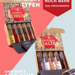 May include: Two open boxes with a variety of small glass jars filled with spices. The top box contains chili flakes and the bottom box contains salts. The boxes are brown with a vintage design and the text "ERLESENE CHILIS" and "ERLESENE SALZE" on the front.