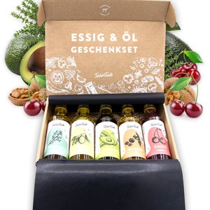 May include: A brown cardboard box with a black lid, containing six small glass bottles of oil and vinegar. The bottles are labeled with different flavors, including avocado, walnut, and cherry. The box is decorated with the text "ESSIG & &Ouml;L GESCHENKSET" and the logo "TimberTaste".