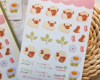 May include: A sheet of stickers featuring cute illustrations of sheep, flowers, birds, and leaves. The stickers are on a pink background with the text "Shelly Flower Field - ICONS SHEET -" at the top. The text "holey! sheep" and "I WOOLY LOVE YOU" are repeated twice on the sheet. The text "SHEEP happens" is also repeated twice on the sheet.