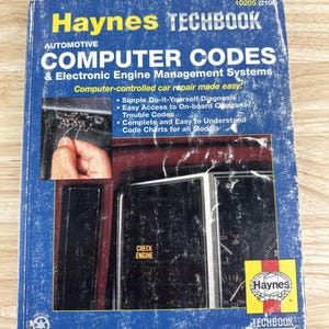 May include: A blue Haynes Techbook titled "Automotive Computer Codes & Electronic Engine Management Systems." The book cover features a photo of a car's dashboard and engine components. Text includes "Computer-controlled car repair made easy!" and "Check Engine."
