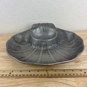 May include: A gray, seashell-shaped serving dish with a central dip bowl. The dish has a ribbed design and is approximately 10 inches wide. A wooden ruler is in the foreground.