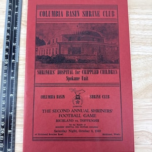 May include: A red vintage program for the Columbia Basin Shrine Club, featuring text and a building illustration. The program promotes a football game between Richland and Toppenish on October 8, 1949, for the benefit of Shriners Hospital for Crippled Children.