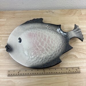 May include: A ceramic fish-shaped serving dish with a white and gray glaze. The fish has a pink belly and black eyes. The dish is approximately 10 inches long.