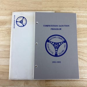 May include: A gray binder and a white booklet with blue text and logos. The binder reads "COMPETITION SANCTION PROGRAM" and "NATIONAL COUNCIL CORVETTE CLUBS, INC. 1981-1982." The booklet is labeled "NCCC HANDBOOK" with a matching logo.