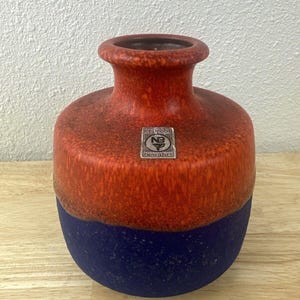May include: A red and blue ceramic vase with a brown label that reads "erprobt" and "bowahrl".