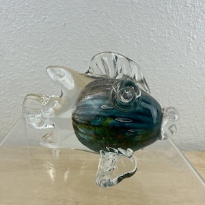 May include: A glass fish figurine with a clear body and a blue, green, and orange swirl pattern. The fish has a clear fin and tail.