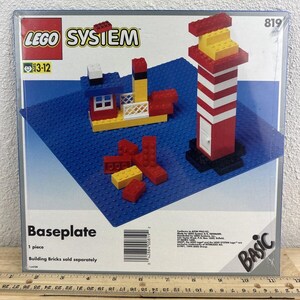 May include: A LEGO set with a blue baseplate, a red and white lighthouse, and a red and yellow boat. The set is labeled "LEGO SYSIEM" and "819".