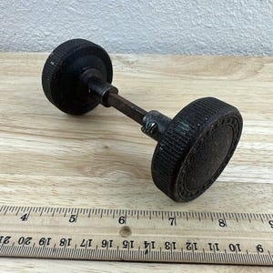May include: A pair of black door knobs with a metal spindle. The knobs are approximately 2 inches in diameter and have a textured surface.