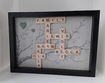 May include: A framed artwork featuring a gray background with a floral design. The artwork is made with wooden letter tiles spelling out the names "Family", "Lewis", "Bryan", "Becca", and "Ella".