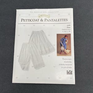 May include: A white package featuring a petticoat and pantalettes pattern from "The American Girls Collection." The package includes an illustration of the garments and a girl in a blue dress. Text on the package reads "Kirsten's Petticoat & Pantalettes."