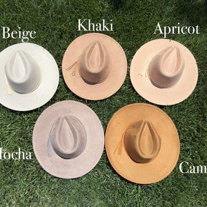 May include: Five fedora hats in neutral shades: beige, khaki, apricot, mocha, and camel. Each hat features a wide brim and a pinched crown. The hats are arranged on green grass, with the colour names displayed above each hat.