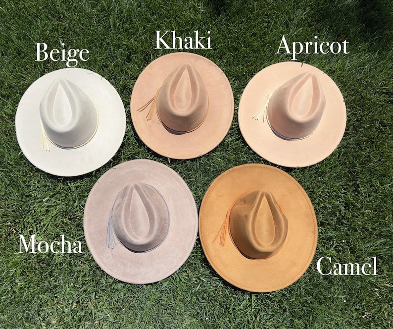 May include: Five fedora hats in neutral shades: beige, khaki, apricot, mocha, and camel. Each hat features a wide brim and a pinched crown. The hats are arranged on green grass, with the colour names displayed above each hat.