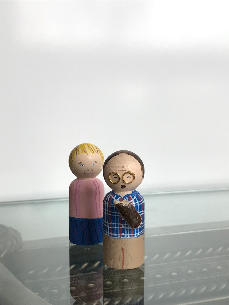 Puede incluir: Dos mu&ntilde;ecas de madera con clavijas, una con cabello rubio que lleva una camisa rosa y pantalones azules, la otra con cabello casta&ntilde;o que lleva una camisa a cuadros azules y blancos y sostiene un objeto marr&oacute;n.