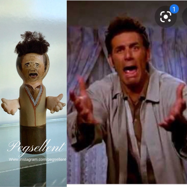 May include: A wooden peg doll with a painted face and brown hair. The doll is wearing a brown shirt with a white collar and a brown vest. The doll is holding its arms out to the sides. The doll is standing on a wooden base. The text "Pegsellent" and "www.instagram.com/pegsellent" is visible below the doll.