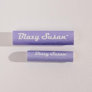 May include: Two purple Blazy Susan rolling trays. The larger tray is in the background and the smaller tray is in the foreground. Both trays have the text "Blazy Susan" printed in white.