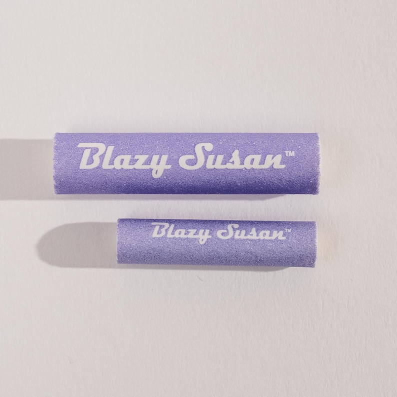 May include: Two purple Blazy Susan rolling trays. The larger tray is in the background and the smaller tray is in the foreground. Both trays have the text "Blazy Susan" printed in white.