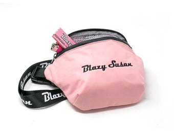 May include: A pink fanny pack with a black adjustable strap and the text "Blazy Susan" embroidered on the front.