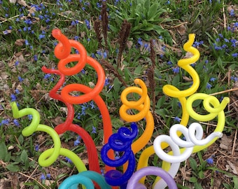 Könnte beinhalten: Eine Regenbogen-Skulptur aus Glas in einer Gartenlandschaft. Die Skulpturen bestehen aus buntem Glas und sind spiralförmig. Sie sind in der Mitte des Bildes in einer Gruppe angeordnet.