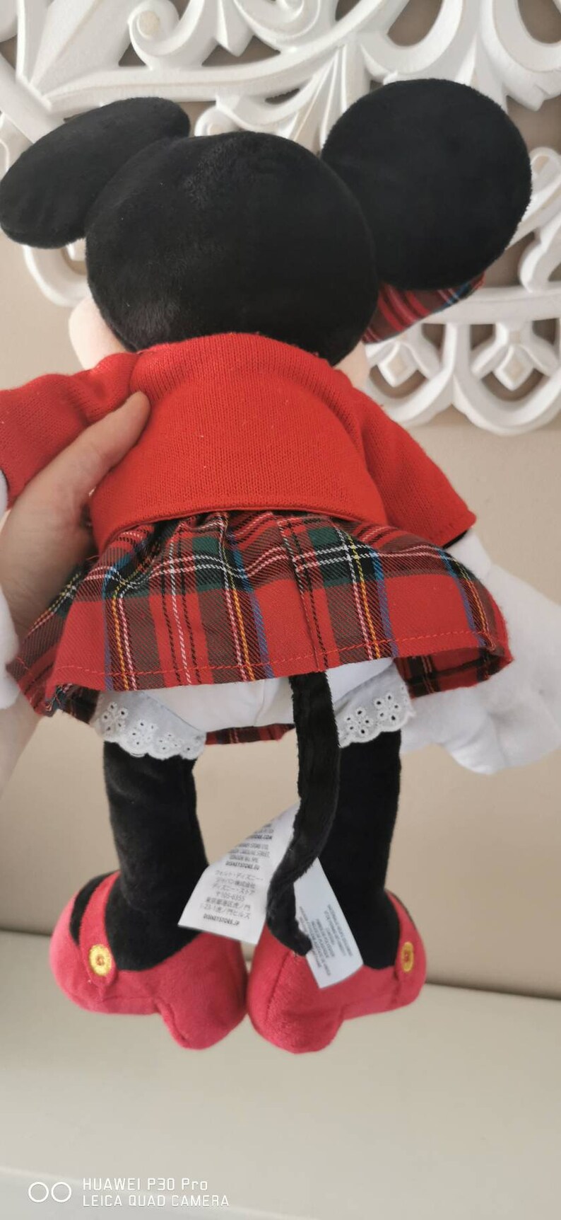 May include: A red and black plush toy of Minnie Mouse wearing a red sweater and a red and black plaid skirt. The toy has a white lace trim on the skirt and black shoes with red accents.