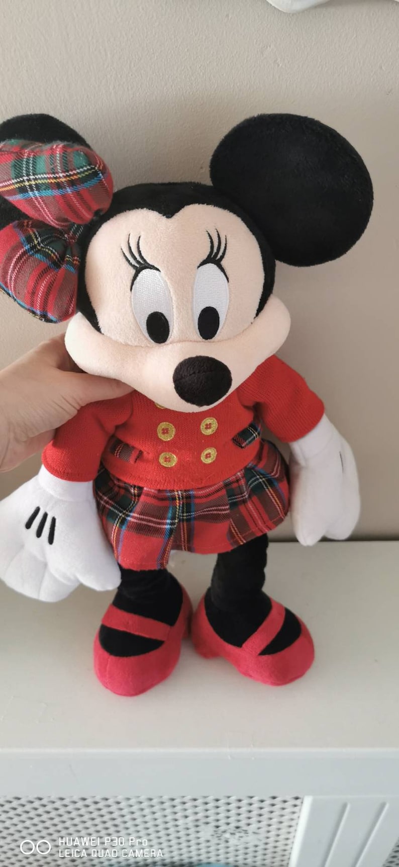May include: A red and black plaid Minnie Mouse plush toy wearing a red dress with gold buttons and black shoes.