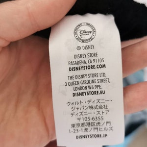 May include: White tag with black text listing the Disney Store locations in Pasadena, California, London, England, and Tokyo, Japan. The tag also includes the website addresses disneystore.com, disneystore.eu, and disneystore.jp.
