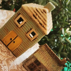 May include: Two small ceramic houses, one green with a yellow door and the other brown with a textured roof, are sitting on a patterned surface.