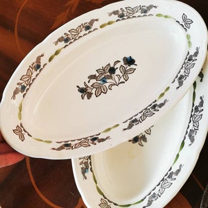 May include: Two white oval serving dishes with a green and black floral design. The dishes have a raised rim and a scalloped edge.