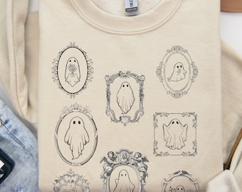 Puede incluir: Una sudadera beige con un estampado gráfico de fantasmas en marcos ornamentados. Los fantasmas son blancos y los marcos son negros. La sudadera es de cuello redondo.